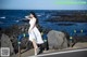 A woman in a white dress leaning against a railing by the ocean.