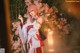 A woman in a kimono standing in front of a bunch of flowers.