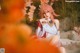 A woman with pink hair sitting on a rock in front of flowers.