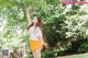 A woman in a white shirt and yellow skirt standing under a tree.