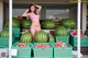 A woman in a pink bikini standing next to a pile of watermelons.